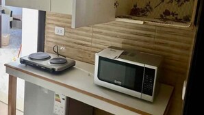 Kompakti keittiö, jossa on mikroaaltouuni, pieni jääkaappi ja saranoilla varustettu ovi, jonka takana on kaappi.