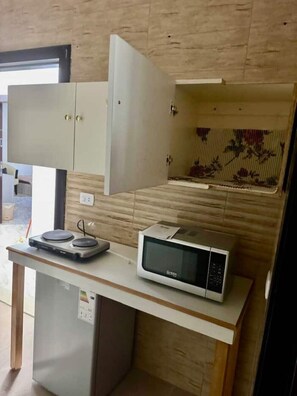 A compact kitchen with a microwave, a small refrigerator, and a cabinet with a hinged door. - Studio flat in a Safe Area - near Khalidi Hospital - Minutes from City Center (Amman)