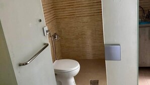 Kylpyhuone, jossa on valkoinen wc-istuin, suihkutila ja selvästi näkyvissä oleva ovenkahva.