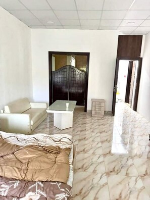 A hotel room with a bed, a sofa, a small table, and a door with a decorative panel. - Studio flat in a Safe Area - near Khalidi Hospital - Minutes from City Center (Amman)