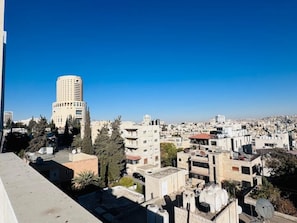 A cityscape with a prominent cylindrical building in the center, surrounded by residential buildings and trees. - Studio flat in a Safe Area - near Khalidi Hospital - Minutes from City Center (Amman)