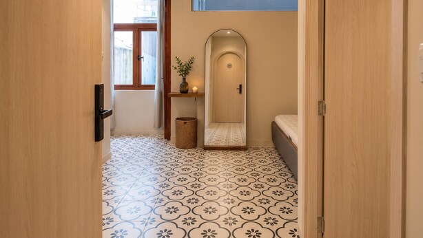 A hallway with patterned flooring, a door with a number plaque, a hanging light fixture, and a small plant on a shelf. - Zen Living (Ho Chi Minh City)