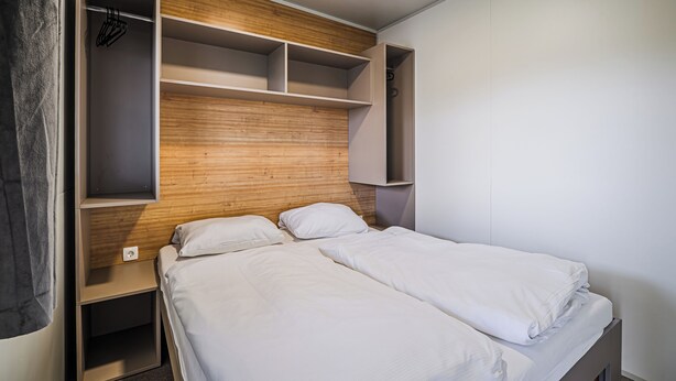 Un dormitorio con una cama, cabecera de madera, armario y estantería.