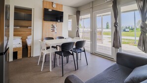 Una habitación moderna con comedor, televisor de pantalla plana en la pared y un ventanal con cortinas.