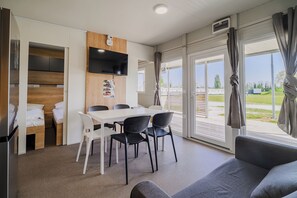 A modern room with a dining area, a flat-screen TV mounted on the wall, and a large window with curtains. - AlpeAdriaBooker Mobile Homes (Čatež ob Savi)
