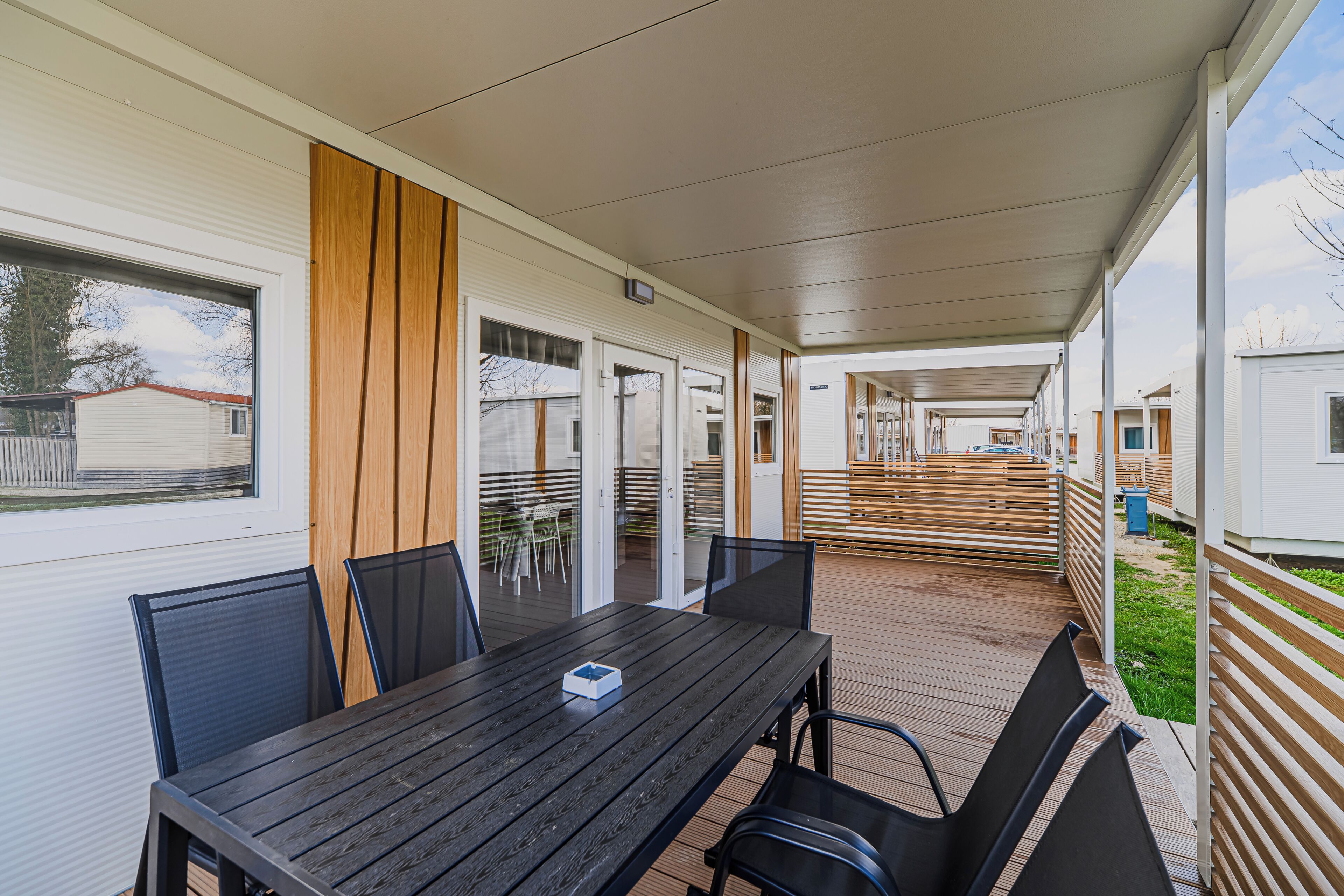 A covered outdoor area with a table and chairs, wooden slats, and a view of adjacent buildings.