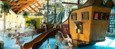 Parque acuático interior con zona de juegos temática de piratas, que incluye un tobogán y una estructura con forma de barco.
