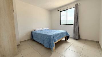 Ein Zimmer mit einem Bett, einem Fenster mit Vorhängen und Blick auf den Himmel.