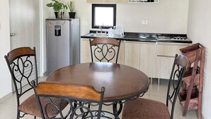 A dining area with a round table and four chairs, a kitchen with wooden cabinets, a refrigerator, and a window.