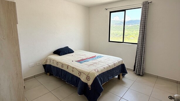 A bedroom with a bed, a window with curtains, and a view of greenery outside.
