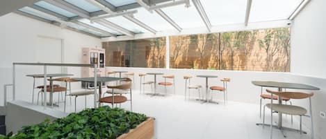 Un espacio interior moderno con varias mesas y sillas, un jardín vertical con plantas y vistas a árboles a través de amplias ventanas.
