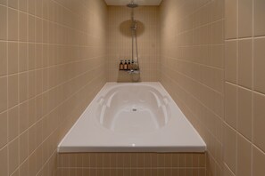 A bathroom with a bathtub, a showerhead, and a shelf with toiletries. - Connected Hotel Nonhyeon (Seoul)