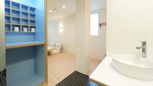 A modern bathroom with a white sink, a blue storage unit with shelves, and a white toilet.