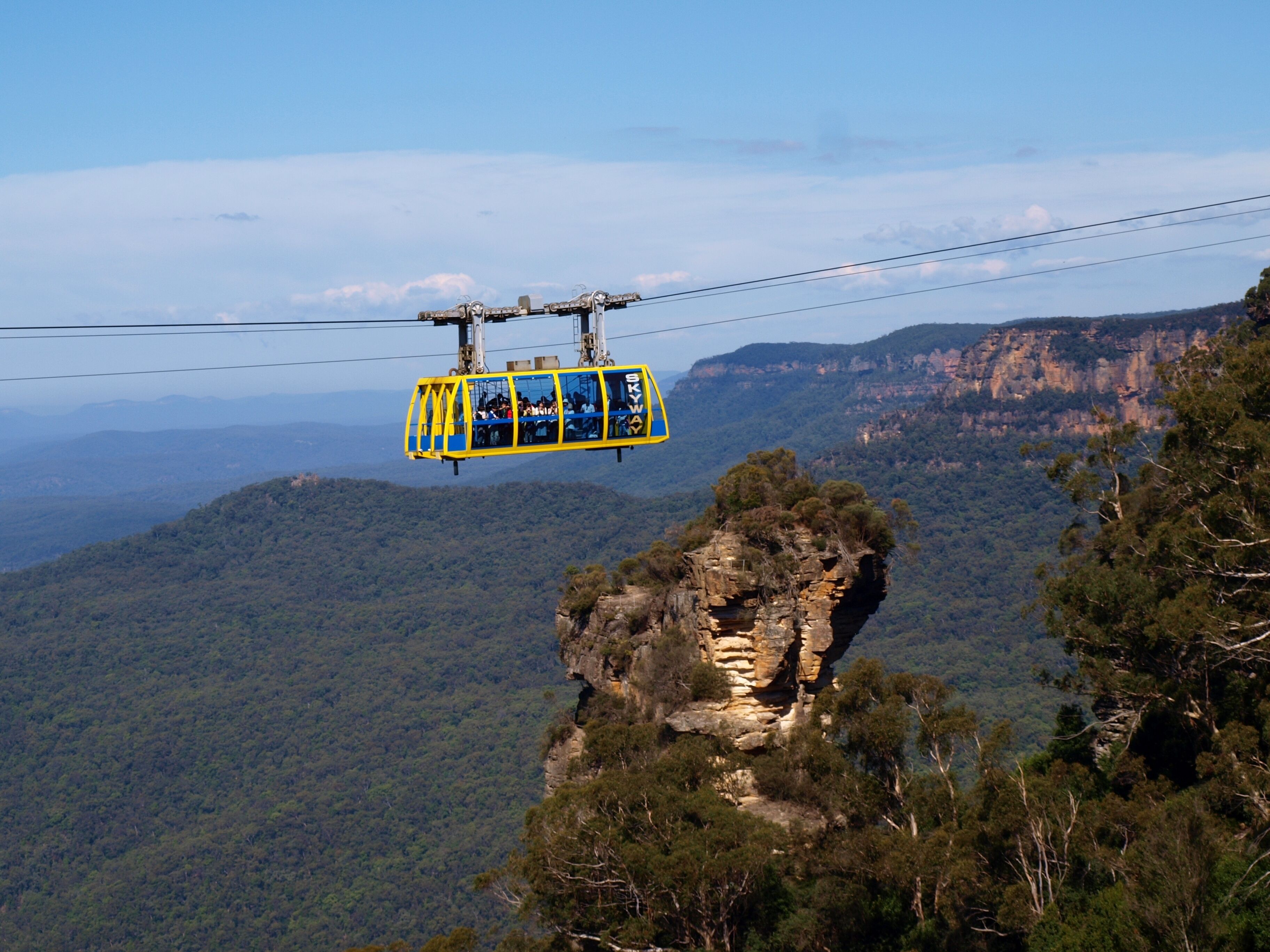 A cable car suspended over a mountainous landscape with dense forest and rocky outcrops.