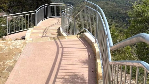 Una escalera metálica que conduce a un mirador con vistas a un valle y montañas a lo lejos.