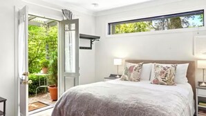 A bedroom with a bed, a nightstand, a window, and an open door leading to a balcony.