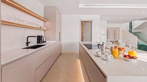 A modern kitchen with a built-in espresso machine, a coffee maker, and a breakfast setup with croissants, fruit, and juice. - VILLA STATUS BY VACATION MARBELLA (Estepona)