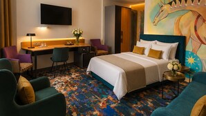 Ett hotellrum med en säng, ett skrivbord, en tv och en färgglad matta.