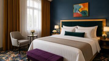 Habitación de hotel con una cama grande, una silla, una mesita con flores y un cuadro abstracto y colorido en la pared.