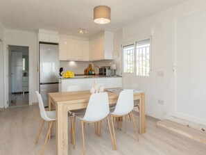A modern kitchen with white cabinets, a wooden dining table, and white chairs. - Alondras by Interhome (Peñiscola)
