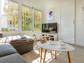 Un salon moderne comprenant un canapé, un téléviseur, une petite table avec des tasses et une assiette, et une bibliothèque.