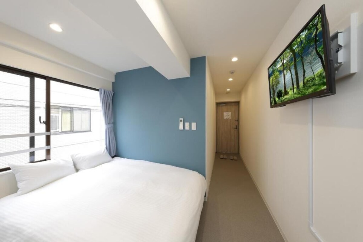 Une chambre d’hôtel avec un grand lit, un téléviseur fixé au mur et une fenêtre avec des rideaux.