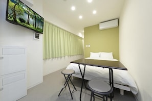 Una habitación de hotel con cama, escritorio, silla, televisor en la pared y ventana con cortinas.