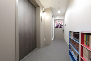 Un couloir avec une porte fermée, un interrupteur et un luminaire fixé au mur.
