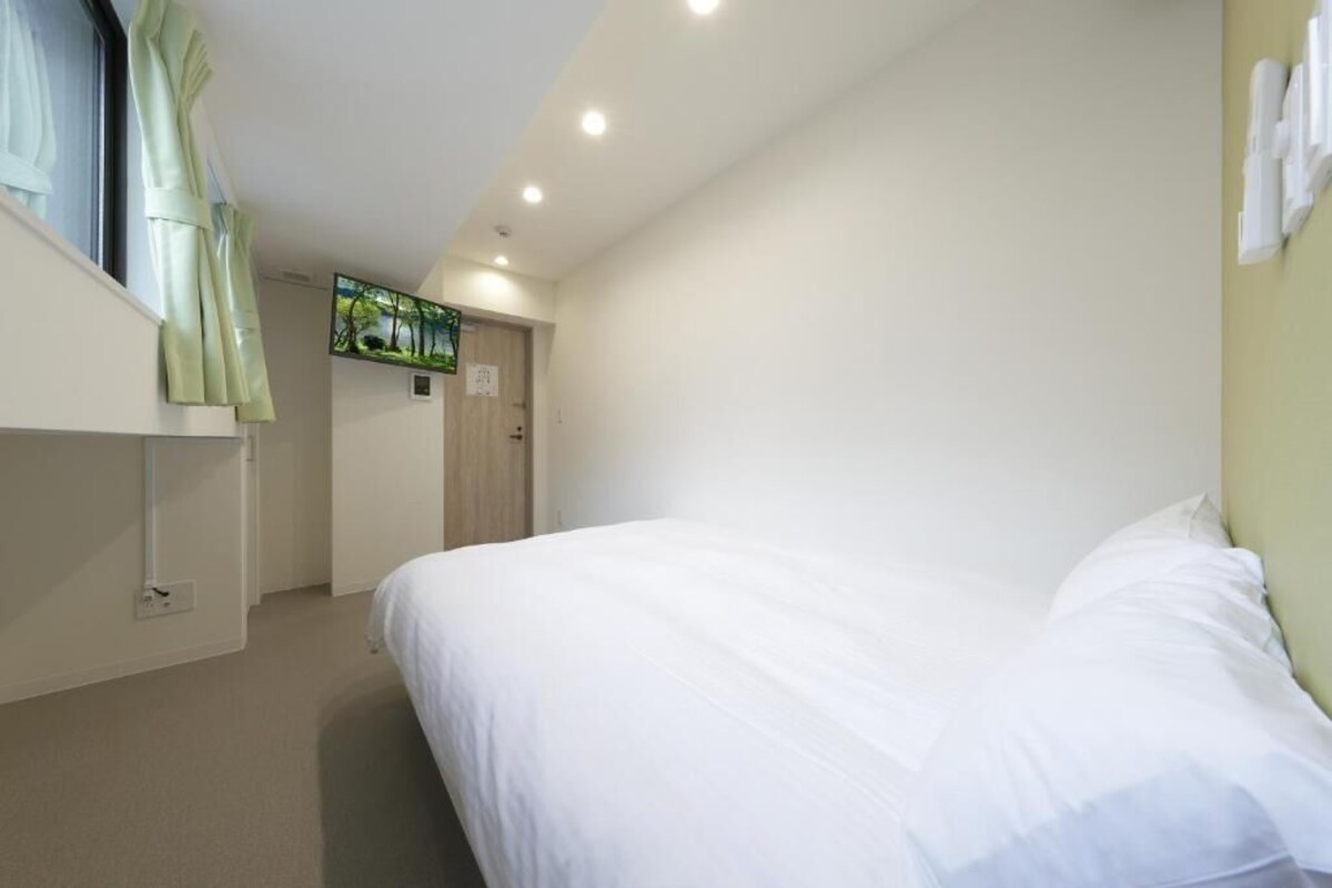 Une chambre d’hôtel avec un lit, une fenêtre avec des rideaux, une porte et une œuvre d’art accrochée au mur.