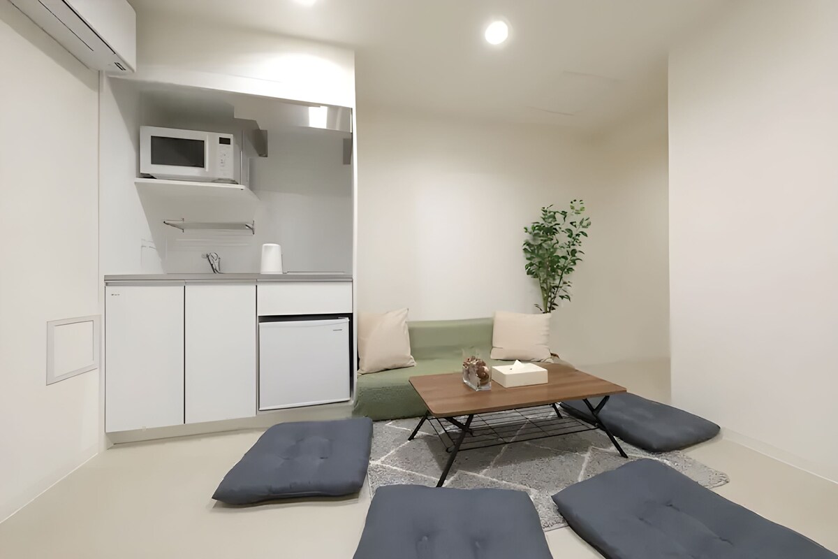 Un espace de vie compact comprenant un coin cuisine, un canapé, une table basse et une plante en pot.