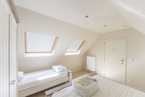 Un dormitorio con dos camas, un tragaluz, un radiador y una puerta.