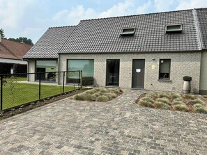 Un bâtiment moderne avec une façade en briques, de grandes fenêtres et un espace d’entrée pavé.
