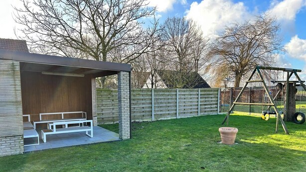 A covered outdoor seating area with benches, a swing set, and a fenced play area.