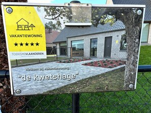 A signboard with a house icon and five stars, indicating a five-star rating, and the text 'de kwetshage' suggesting the name of the property.