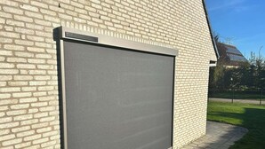 A large, closed roller door attached to a brick wall, with a clear sky and a grassy area in the background.
