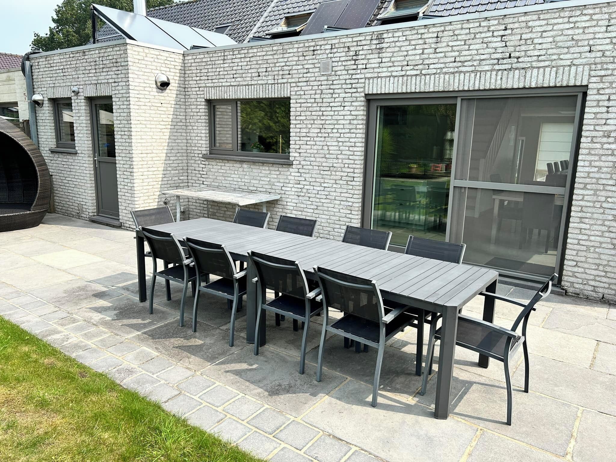 Un patio al aire libre con una mesa rectangular y sillas, un muro de ladrillo y un amplio ventanal corredero.