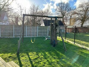 A backyard with a swing set, a wooden fence, and a grassy lawn.
