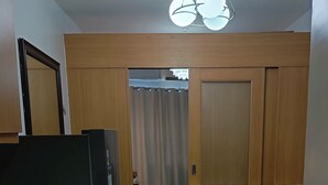 A compact living space with a kitchenette, a sofa with cushions, a dining table, and a ceiling light fixture. - Enjoyable 1-bedroom condo with AC in Pasay City (Pasay City)