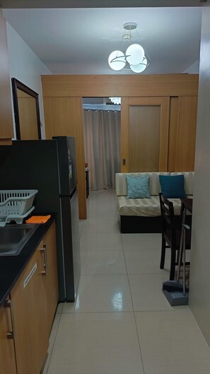 A compact living space with a kitchenette, a sofa with cushions, a dining table, and a ceiling light fixture. - Enjoyable 1-bedroom condo with AC in Pasay City (Pasay City)