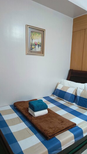 A bed with a checkered bedspread, a brown blanket, and a folded towel. - Enjoyable 1-bedroom condo with AC in Pasay City (Pasay City)