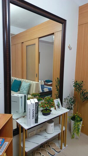 A room with a large mirror, a bedside table with books, a potted plant, and a bed with pillows. - Enjoyable 1-bedroom condo with AC in Pasay City (Pasay City)