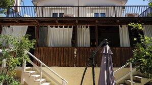 Un edificio de dos pisos con balcón, terraza de madera y escalera que lleva al nivel superior.