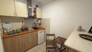 Cocina compacta con lavavajillas, armarios de madera, un lavamanos y una zona de comedor con mesa y sillas.