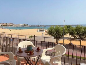 Ein Balkon mit Tisch und Stühlen mit Blick auf Strand und Hafen.