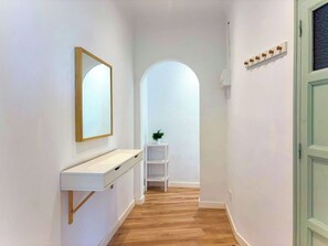 En gang med et hvidt toiletbord, et spejl, en plante og en dør med en lyskontakt.