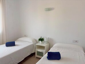 A room with two single beds, a nightstand with a lamp and a plant, and a power outlet on the wall. - Apartment Aubí by Interhome (Palamós)
