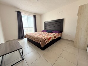 Une chambre à coucher avec un lit, une table de chevet, une fenêtre avec des rideaux et une vue sur l’extérieur.