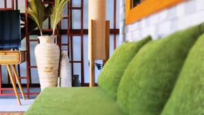 Um sofá verde em um quarto com uma cadeira de madeira, um vaso alto com plantas e um espelho grande na parede.