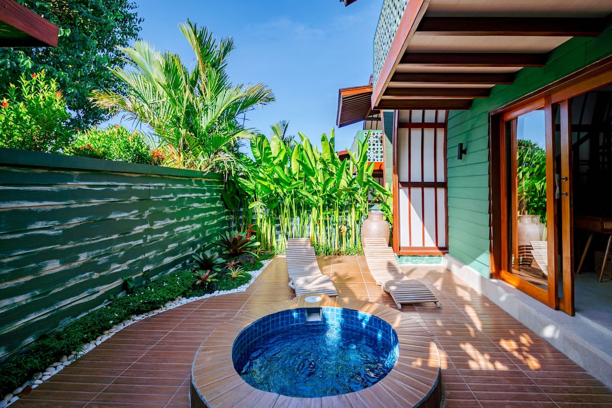 A swimming pool with a wooden deck, surrounded by lush greenery and a traditional building with sliding doors.