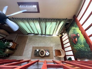 A room with a ceiling fan, a window with curtains, a painting, a wooden floor, and a staircase. - eywa retreat bali (Ungasan)